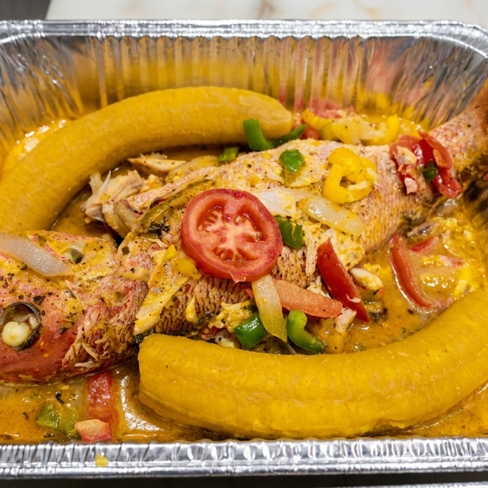 Seasoned fish with plantains, tomatoes, peppers, and onions in a savory sauce, served in a foil tray.