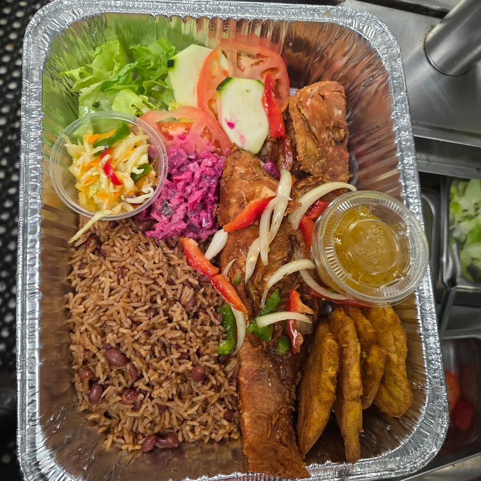 Aluminum tray filled with rice and beans, fried plantains, grilled meat, vegetables, salad, slaw, and dipping sauce.