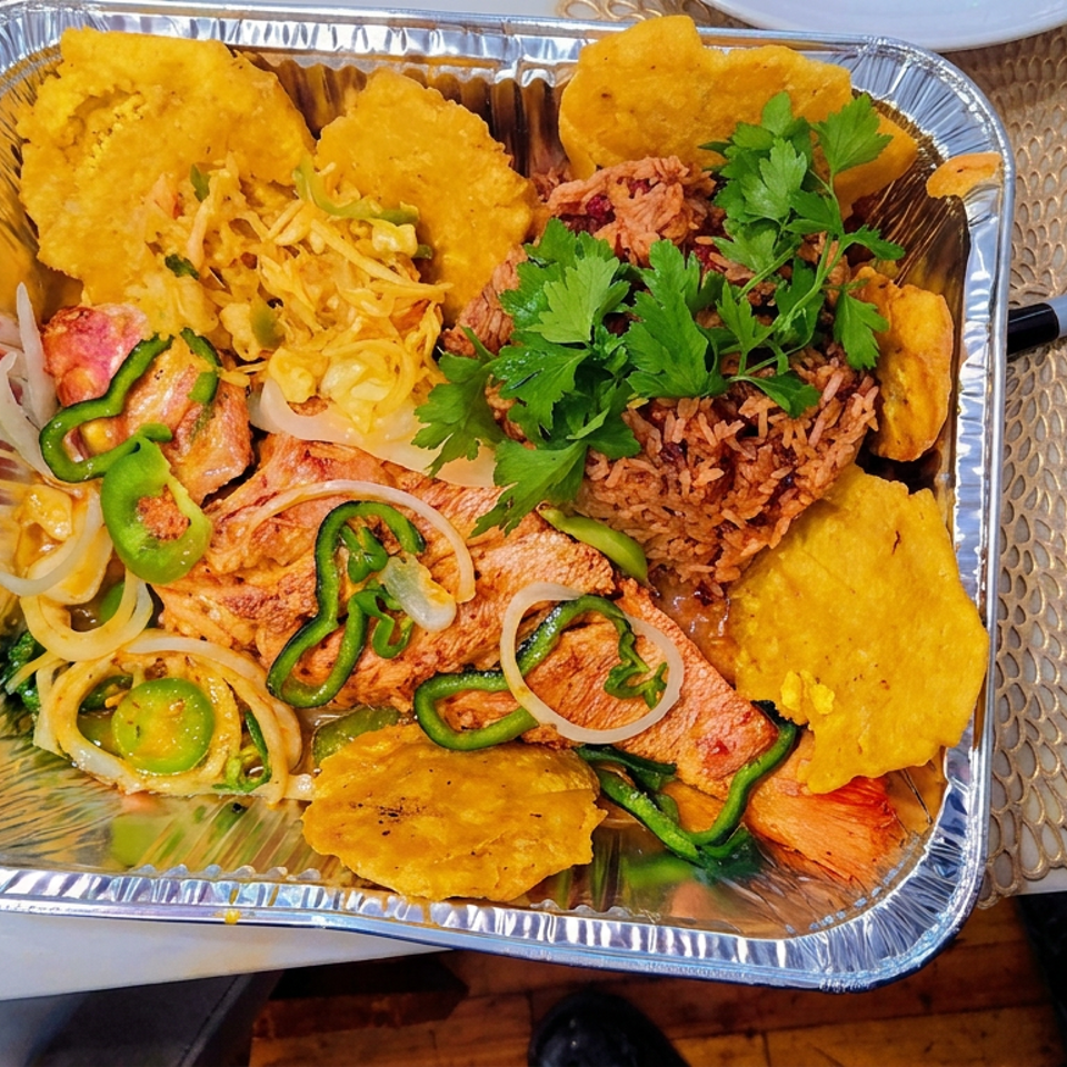 Aluminum takeout tray holds grilled meat, seasoned rice, fried plantains, sautéed onions and peppers, shredded cabbage, and fresh parsley.