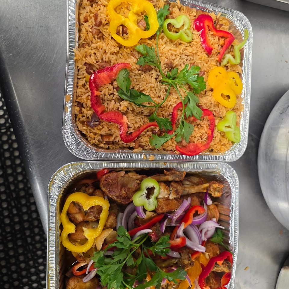 Two foil catering trays hold seasoned rice and roasted chicken, garnished with colorful peppers, red onion, and fresh parsley.