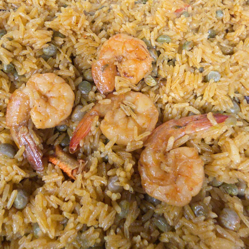 Close-up of seasoned rice mixed with green peas and several cooked shrimp.