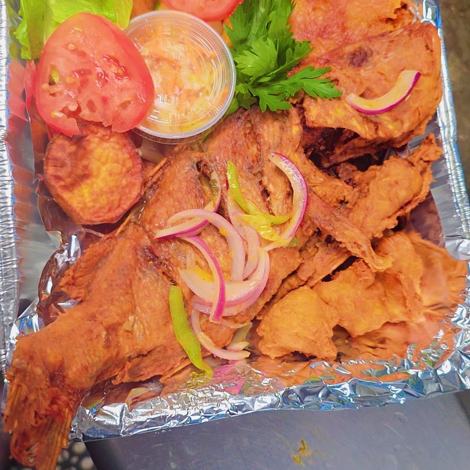 Foil-lined platter of fried fish and shrimp with lettuce, tomatoes, pickles, parsley, onions, and dipping sauce.