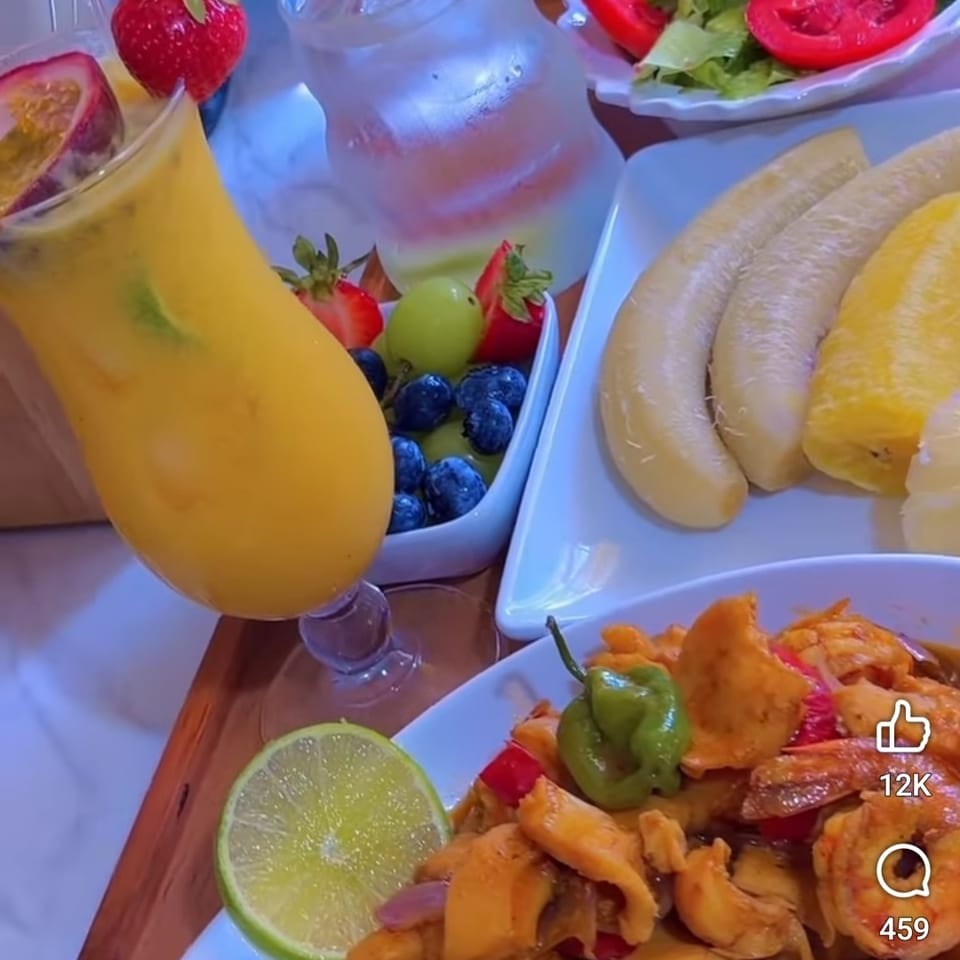 Colorful tropical feast featuring orange juice, fresh fruit, salad, bananas, and a seafood dish garnished with lime.